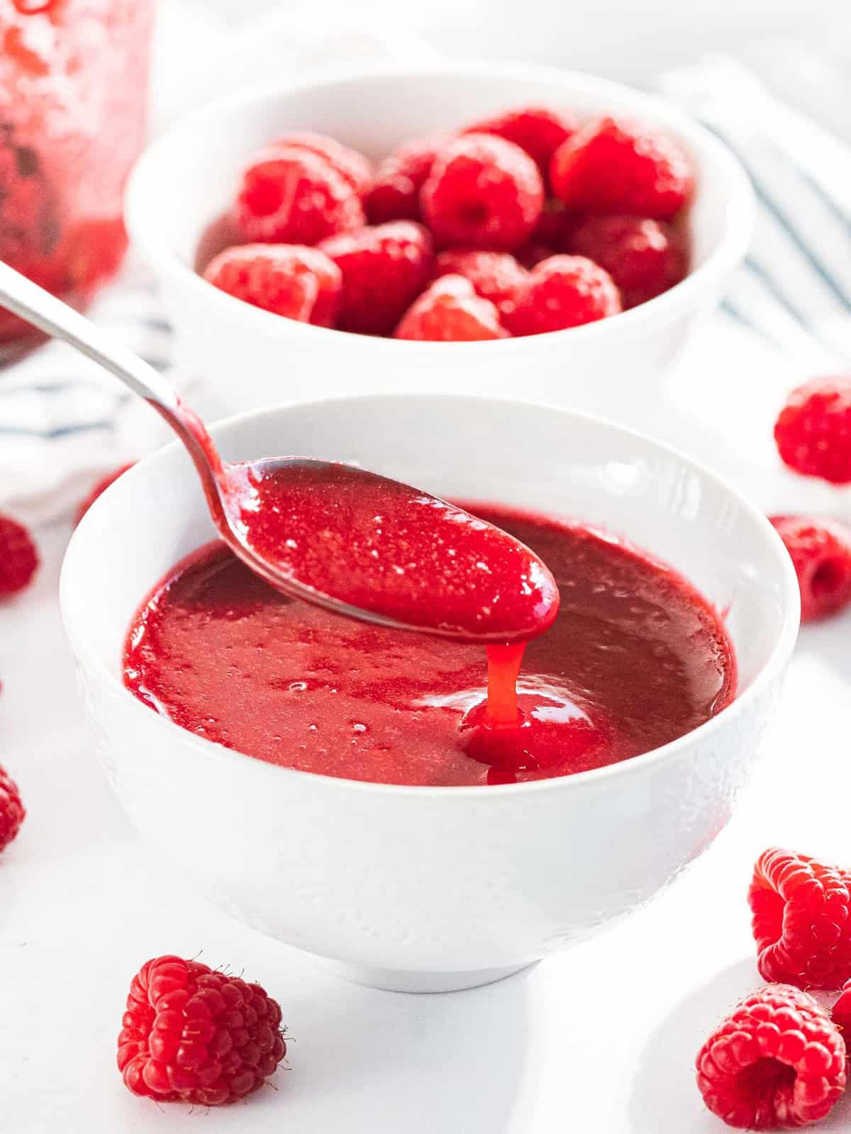 Raspberry sauce or raspberry coulis drizzled off a spoon into a bowl.