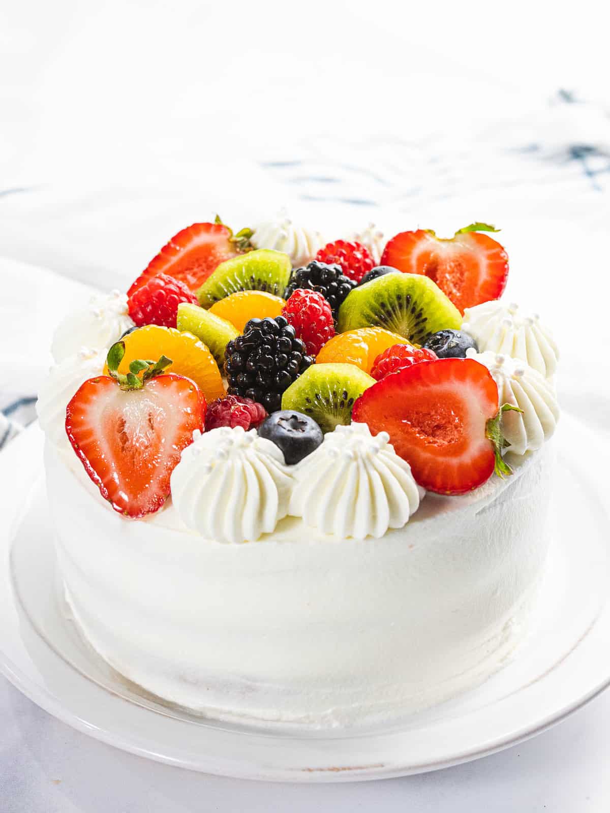 Fresh fruit cake topped with strawberries, kiwi, berries, and whipped cream.