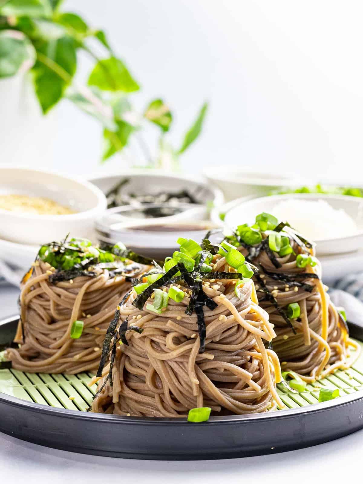 Portions of cold soba noodles topped with nori, green onions, and sesame seeds.
