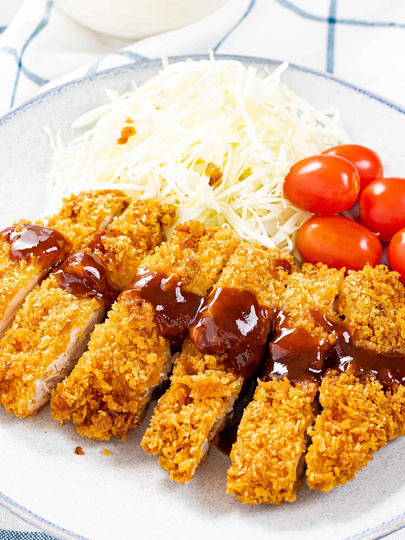 The best chicken katsu with crispy breadcrumbs next to shredded cabbage and tomatoes.