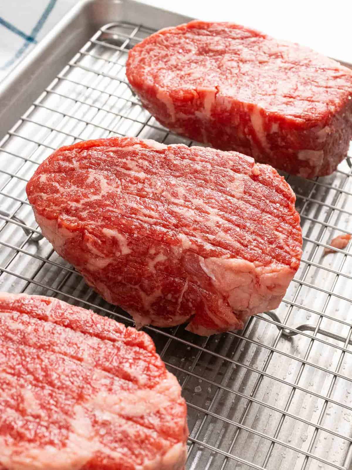 Thick-cut ribeye steaks on a baking rack.