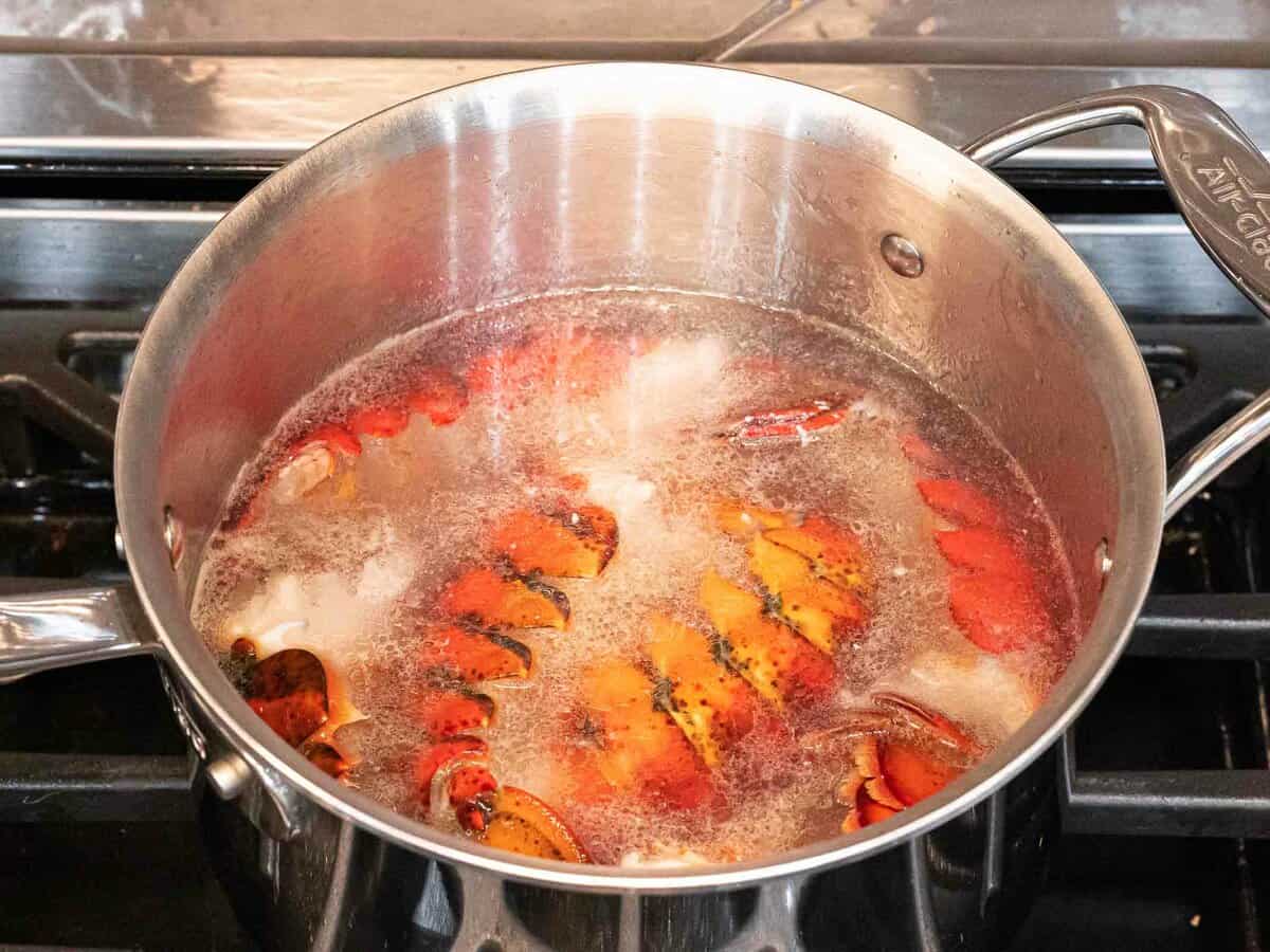 Lobster shells boiling with onions, carrots, and celery in a large pot.