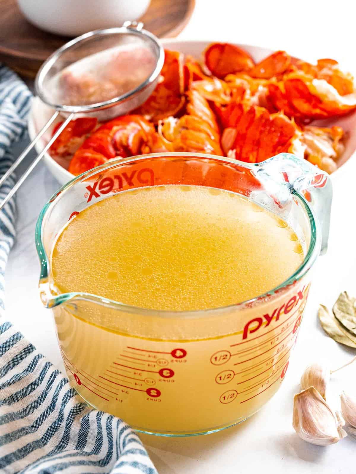Lobster stock in a glass container in front of red lobster shells.