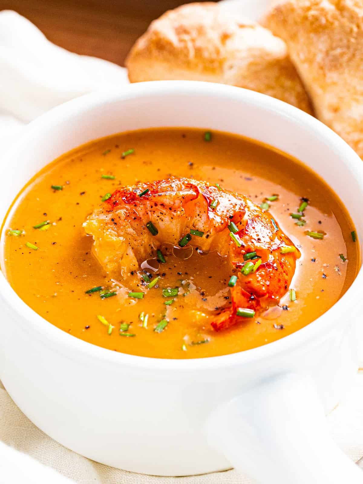 A bowl of lobster bisque garnished with buttered lobster tail and chives.