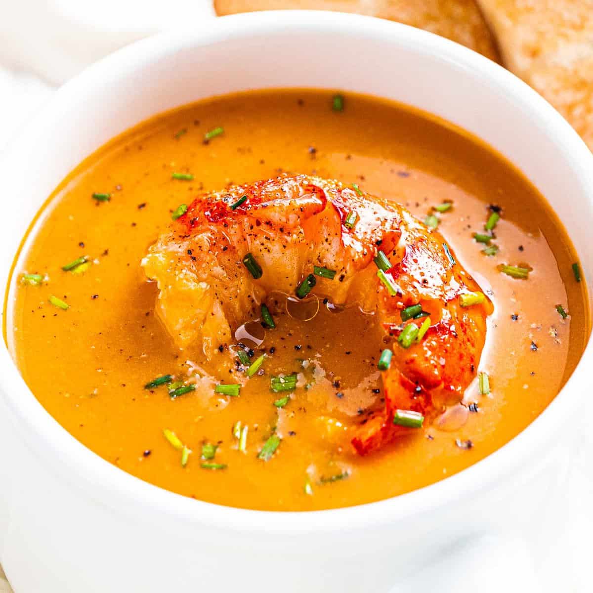 Lobster bisque with lobster tail and chives in a white bowl.