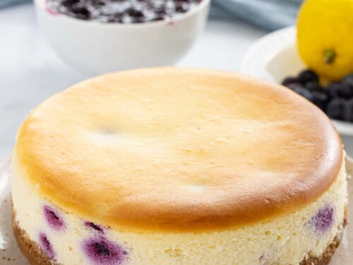 Blueberry cheesecake no cracks next to a bowl of blueberry sauce.