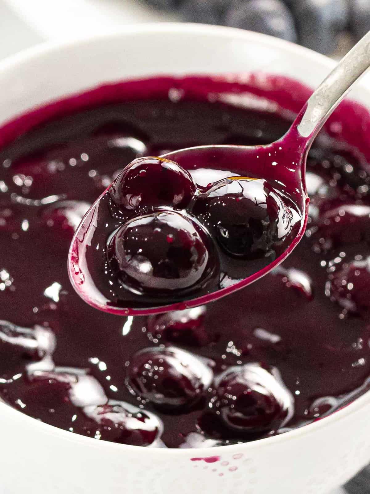 Blueberry compote with pieces of blueberries on a spoon.