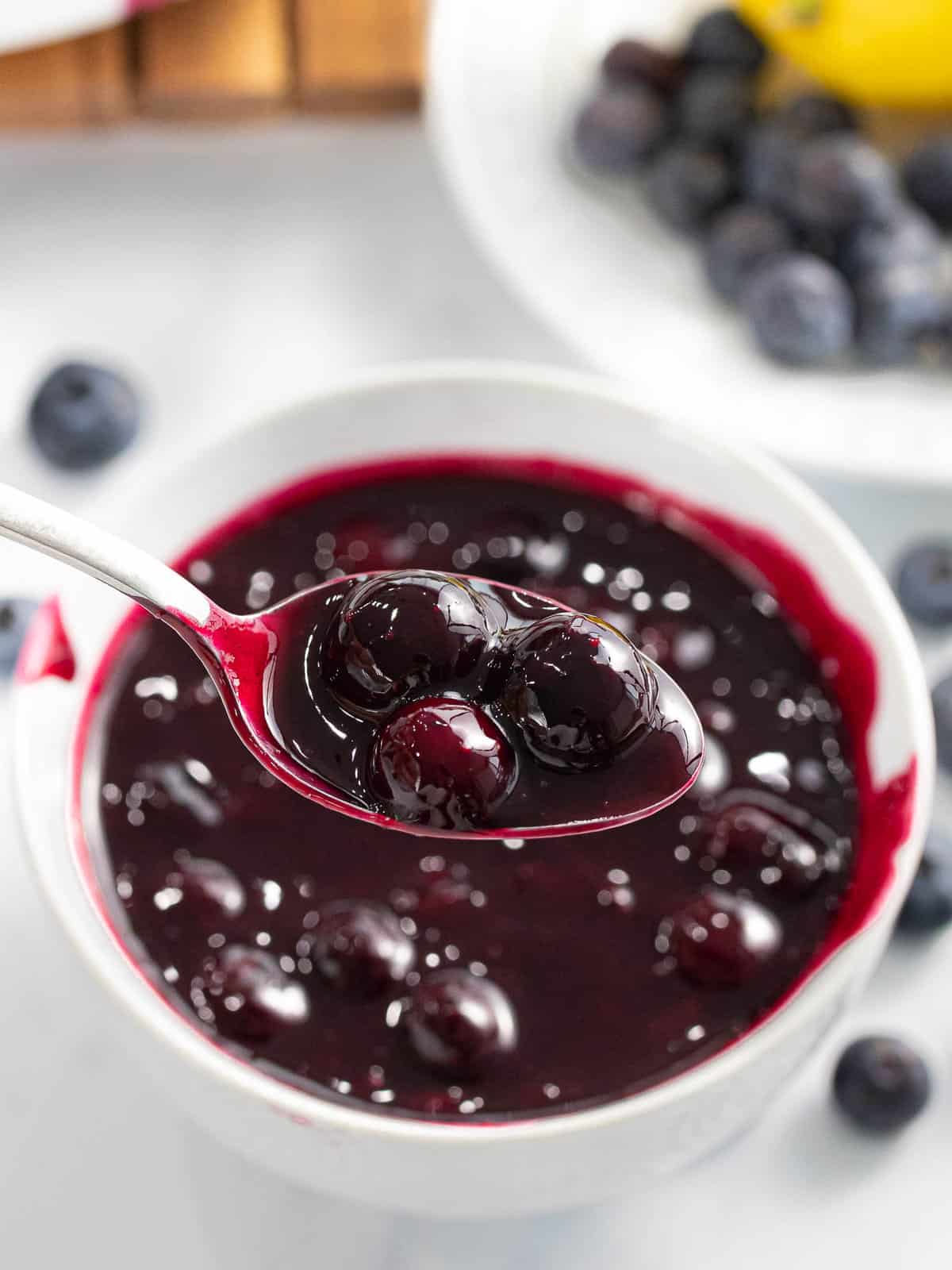 Blueberry compote served on a spoon with fresh blueberries.